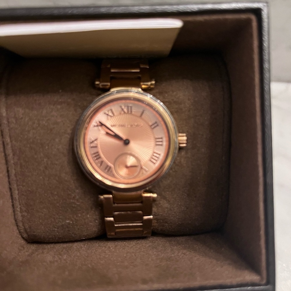 Micheal Kors woman’s rose gold watch with metal band.